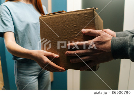 Close-up side view of woman customer receiving cardboard box parcel at home from delivery man hands on doorway. Closeup of courier male delivering to female customer package post to apartment. Close-up side view of woman customer receiving cardboard box parcel at home from delivery man hands on doorway. Closeup of courier male delivering to female customer package post to apartment. 86900790