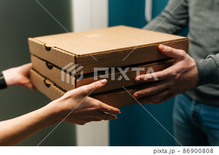 Close-up cropped shot of woman customer receiving carton boxes with pizza at home from delivery man hands. Closeup side view of courier male delivering to female customer food at home. Close-up cropped shot of woman customer receiving carton boxes with pizza at home from delivery man hands. Closeup side view of courier male delivering to female customer food at home. 86900808