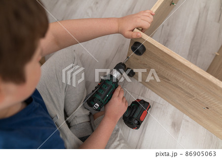 A young boy is tightening screws with a cordless screwdriver. A young boy is tightening screws with a cordless screwdriver. 86905063