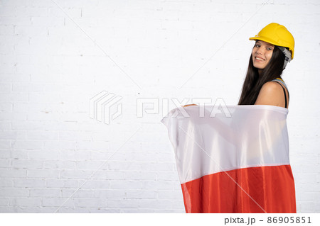 A young construction worker covered herself with the national flag of Poland. A woman in the profession of a builder. 86905851