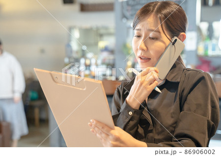 スマホで連絡を取る多忙な女性店員 86906002