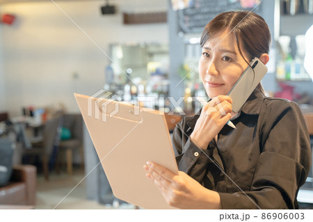 スマホで連絡を取る多忙な女性店員 スマホで連絡を取る多忙な女性店員 86906003