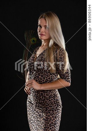 Young girl stands on black background and in her hands she holds peacock feather. She is blonde with long hair. Young girl stands on black background and in her hands she holds peacock feather. She is blonde with long hair. 86906344