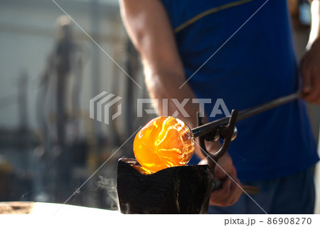 Close-up of the hands of a master glassblower working with molten glass Traditional handmade crafts. Close-up of the hands of a master glassblower working with molten glass Traditional handmade crafts. 86908270