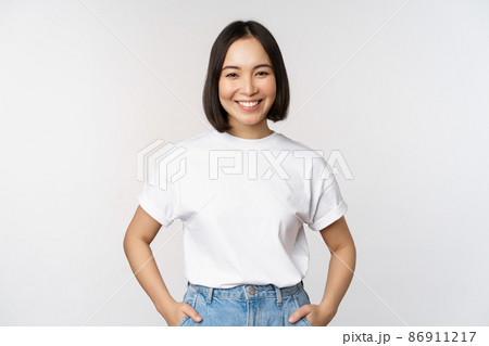 Lifestyle. Happy modern asian girl, smiling and looking happy at camera, posing in white tshirt and jeans, studio background Lifestyle. Happy modern asian girl, smiling and looking happy at camera, posing in white tshirt and jeans, studio background 86911217