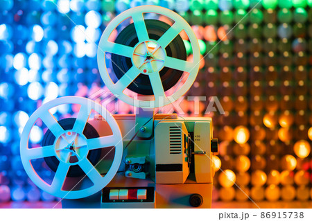 Retro reel with film rotating on colorful shining sparkles wall. Old-fashioned 8mm film projector 86915738