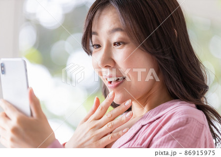 明るい室内でスマホの画面を見る部屋着姿の女性 86915975
