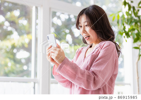 明るい室内でスマホの画面を見る部屋着姿の女性 86915985