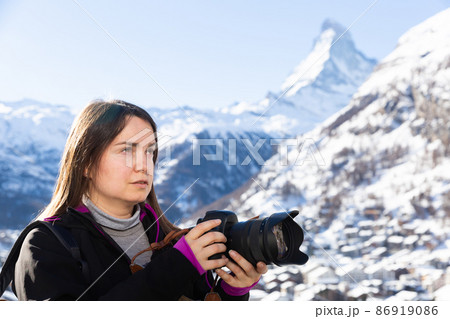 Photographer woman with camera taking pictures of winter Swiss Alps 86919086