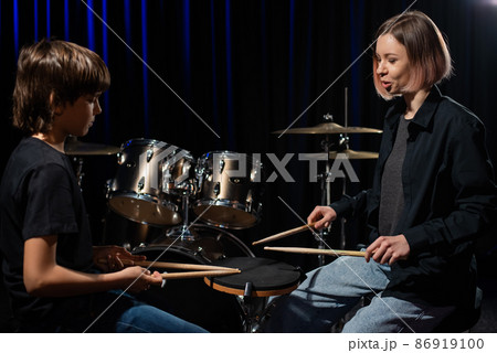 Young caucasian woman teaches a boy to play the drums in the studio on a black background. Music school student Young caucasian woman teaches a boy to play the drums in the studio on a black background. Music school student 86919100