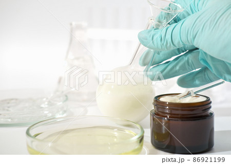 hand in rubber medical glove holding laboratory glassware with fermented cosmetic product, face cream with enzymes developed in a lab.  86921199