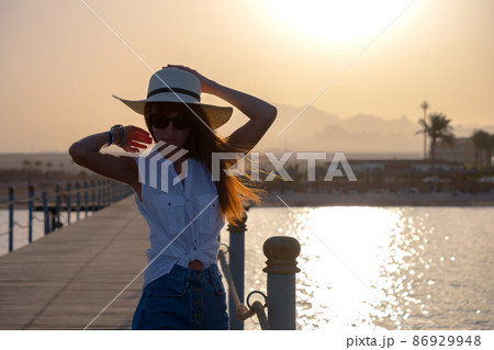Young happy woman tourist relaxing outdoors on warm sunny evening on sea shore. Summer vacations and travelling concept. Young happy woman tourist relaxing outdoors on warm sunny evening on sea shore. Summer vacations and travelling concept. 86929948