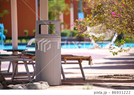 Empty deck chairs under straw shade umbrellas on swimming pool side and litter bin for garbage disposal in tropical resort. Summer vacations and getaway concept 86931222