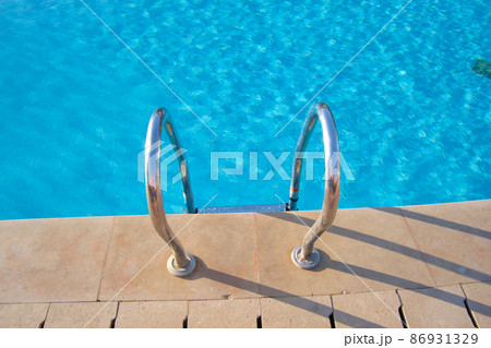 Close up of swimming pool stainless steel handrail descending into tortoise clear pool water. Accessibility of recreational activities concept. 86931329