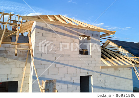 Aerial view of unfinished frame of private house with aerated lightweight concrete walls and wooden roof frame under construction. Aerial view of unfinished frame of private house with aerated lightweight concrete walls and wooden roof frame under construction. 86931986