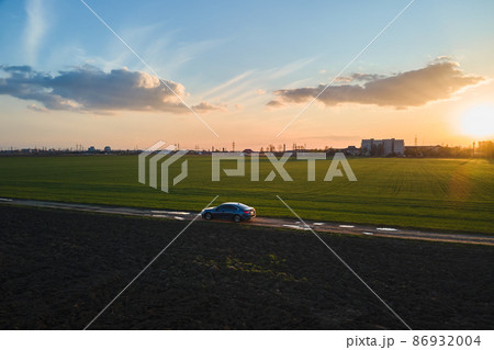 Aerial view of sedan car driving fast on dirt road at sunset. Traveling by vehicle concept. Aerial view of sedan car driving fast on dirt road at sunset. Traveling by vehicle concept. 86932004