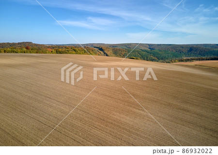 Aerial view of plowed agricultural field with cultivated fertile soil prepared for planting crops in spring Aerial view of plowed agricultural field with cultivated fertile soil prepared for planting crops in spring 86932022