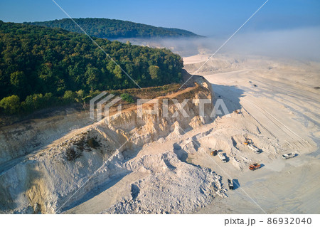 Aerial view of open pit mining site of limestone materials extraction for construction industry with excavators and dump trucks. Aerial view of open pit mining site of limestone materials extraction for construction industry with excavators and dump trucks. 86932040