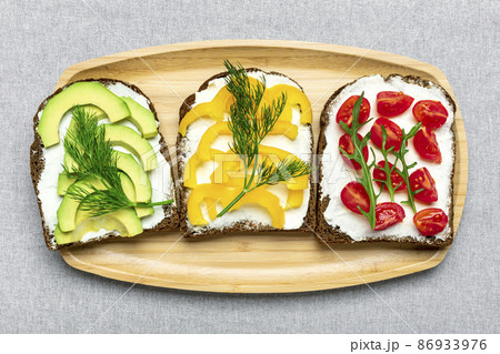 Variety of sandwiches for breakfast - slice of whole grain dark bread, yellow bell pepper, cream cheese, avocado, cherry tomatoes, garnished with dill, green arugula on table Top view Flat lay Variety of sandwiches for breakfast - slice of whole grain dark bread, yellow bell pepper, cream cheese, avocado, cherry tomatoes, garnished with dill, green arugula on table Top view Flat lay 86933976