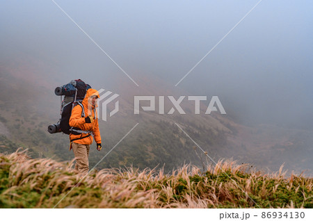 A man climbs a mountain in the fog, a man carries a backpack on his back. 86934130