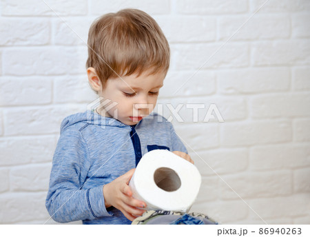 Funny boy sitting on potty chair and playing with toilet paper Funny boy sitting on potty chair and playing with toilet paper 86940263
