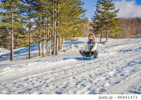 Happy woman having fun during rolling down the mountain slope on sled. Winter sports with snow. People riding a sledge 86941473