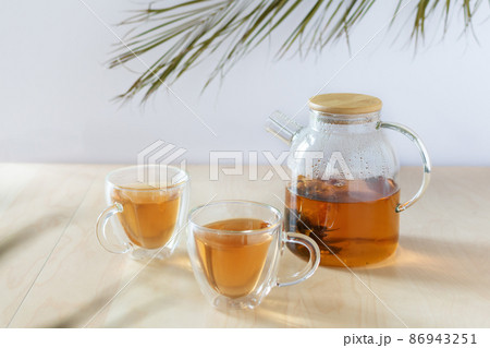 Glass tea pot with flower blooming tea and two tea cups on wooden table. Glass tea pot with flower blooming tea and two tea cups on wooden table. 86943251