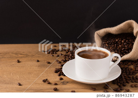 Coffee cup and saucer on wooden background with roasted coffee beans in a burlap sack. 86943287