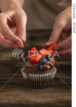 Hands of confectioner decorate cake with fresh berries. Muffin with strawberries and blueberries. Close up cupcake. Hands of confectioner decorate cake with fresh berries. Muffin with strawberries and blueberries. Close up cupcake. 86944934