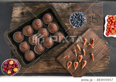 Just Baked Chocolate Muffins In Bakeware and seasonal fruits and berries. Flat lay. Top view. Just Baked Chocolate Muffins In Bakeware and seasonal fruits and berries. Flat lay. Top view. 86944947