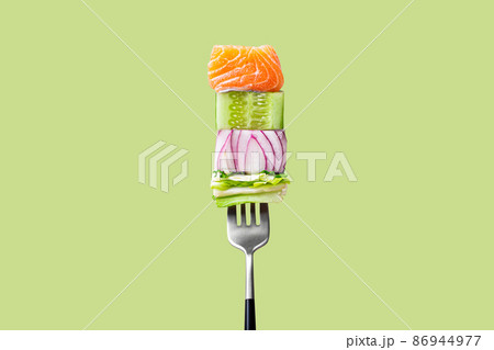 Close-up of fork with food on it: delicious fillet salmon, cucumber, onion, salad on green background Close-up of fork with food on it: delicious fillet salmon, cucumber, onion, salad on green background 86944977