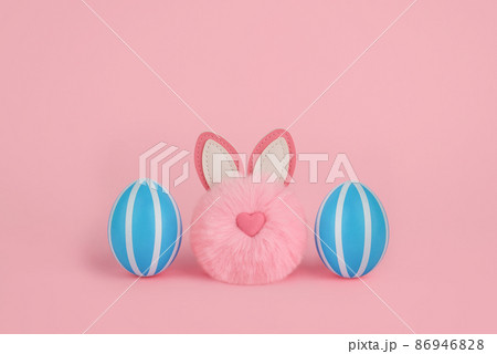 A pink fluffy bunny pom-pom and two blue striped eggs. Easter concept. A pink fluffy bunny pom-pom and two blue striped eggs. Easter concept. 86946828