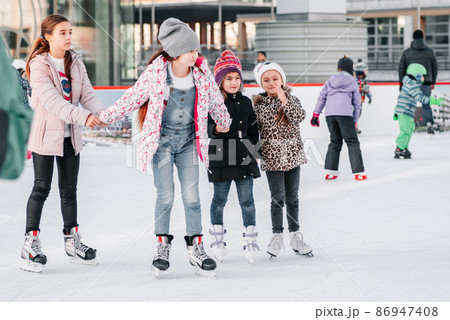 Soft,Selective focus.People, friendship, sport and leisure concept - happy friends on skating rink.Group of teenage friends ice skating on an ice rink.A kid takes relax after his fall while skating. 86947408