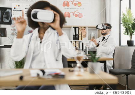 Two multicultural male and female doctors using VR goggles Two multicultural male and female doctors using VR goggles 86948905