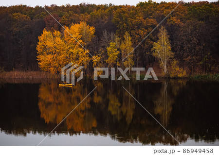 Yellow small boat near the forest with golden autumn trees Yellow small boat near the forest with golden autumn trees 86949458