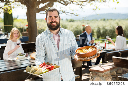 Positive male waiter welcoming guests to country outdoor restaurant 86955298