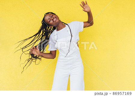 Cheerful woman wearing white overall dancing at yellow wall	 86957169