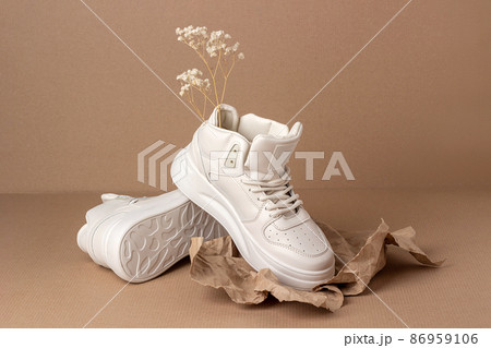 Eco leather shoes. A pair of beige sneakers with dry flowers on brown background. Casual sport lifestyle concept Eco leather shoes. A pair of beige sneakers with dry flowers on brown background. Casual sport lifestyle concept 86959106