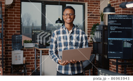 Portrait of african american programer standing working on laptop looking up and smiling Portrait of african american programer standing working on laptop looking up and smiling 86963943