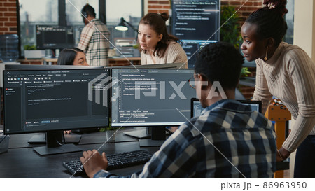 Mixed team of artificial intelligence cloud programers talking about programming in front of multiple screens 86963950