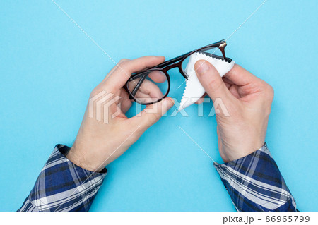 Man wiping glasses for vision with a napkin. Cleaning glasses. Blue background. Flat lay. Top view 86965799
