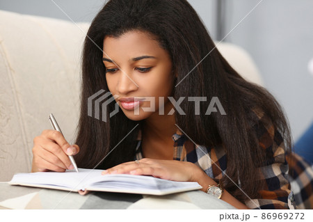 Mulatto girl on the sofa makes notes in the book, close-up 86969272