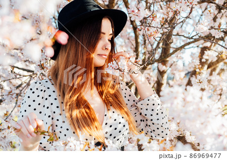 Young brunette woman in hat and dress in white pink blooming tree. Generation Z girl enjoy spring mood during sunny day. Springtime blossom. Selective focus, copy space Young brunette woman in hat and dress in white pink blooming tree. Generation Z girl enjoy spring mood during sunny day. Springtime blossom. Selective focus, copy space 86969477