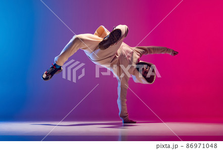 Studio shot of young flexible sportive man dancing breakdance in white outfit on gradient pink blue background. Concept of action, art, beauty, sport, youth 86971048