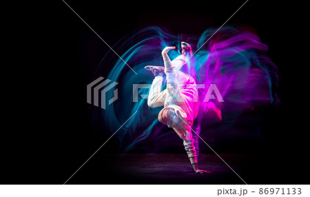 Dynamic portrait of young flexible sportive boy dancing hip-hop or breakdance in white outfit on dark background in mixed pink neon light. Sport, art, action, moves 86971133