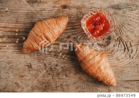 two croissant with strawberry jam on a wooden background, top view. Sweet and hearty breakfast with croissants two croissant with strawberry jam on a wooden background, top view. Sweet and hearty breakfast with croissants 86973549