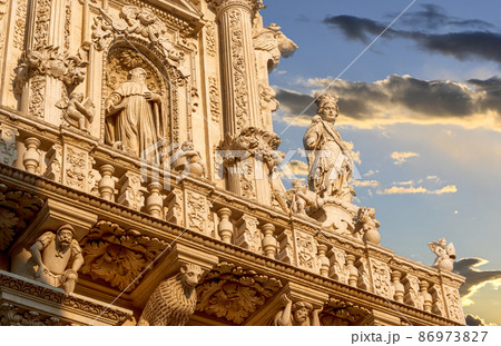 Lecce, Puglia, Italy. August 2021. The church of Santa Croce is the finest example of Lecce baroque. Detail of the facade illuminated by the warm light of the evening. Lecce, Puglia, Italy. August 2021. The church of Santa Croce is the finest example of Lecce baroque. Detail of the facade illuminated by the warm light of the evening. 86973827