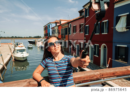 Influence media Burano Italy. Paint building house in Europe Venezia city. Travel photographer blogger girl with smartphone in Venice island color street. Freedom, summer travel, profession concept. 86975645