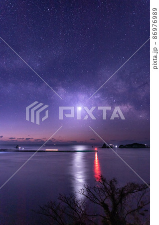 宮崎県日南市池ケ山から七つ岩と並ぶ小場島の上に広がる星空に横に流れる天の川と灯台と共に海を照らす金星 86976989