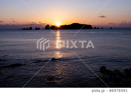 宮崎県日南市大堂津猪崎鼻公園にある猪崎鼻キャンプ場から望む七つ岩と小場島沖合に雲を抑えて昇る朝日 86976991